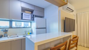 A modern kitchen with a white countertop, wooden chairs, a microwave, and a refrigerator.
