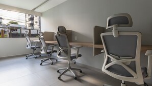 Un espace de bureau moderne comprenant quatre chaises de bureau et un bureau, de grandes fenêtres offrant une vue sur les bâtiments et les arbres, et un aménagement épuré et minimaliste.