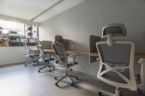 Un espace de bureau moderne comprenant quatre chaises de bureau et un bureau, de grandes fenêtres offrant une vue sur les bâtiments et les arbres, et un aménagement épuré et minimaliste.