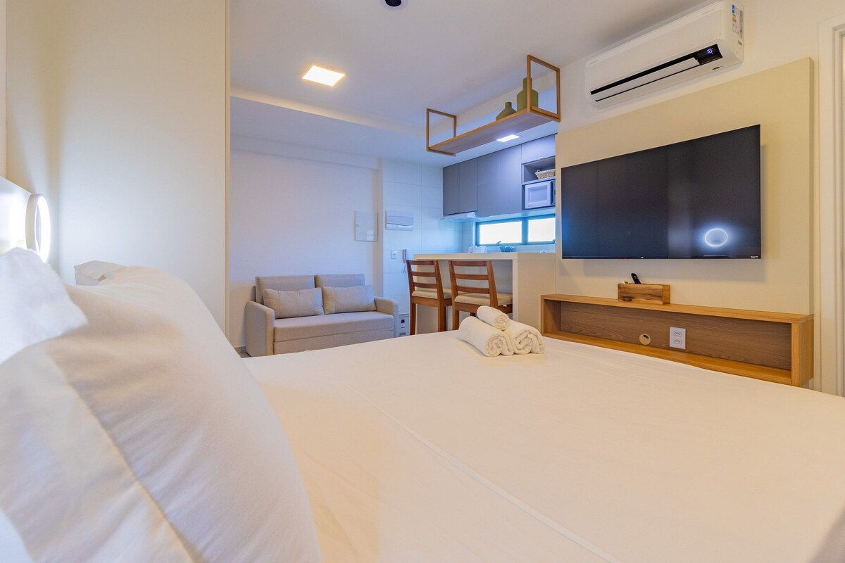 A hotel room with a bed, a TV, a desk, and a kitchenette.