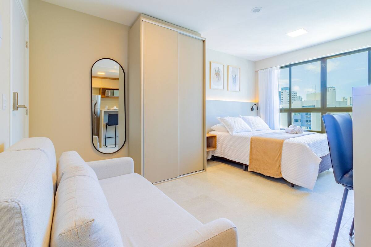 Habitación de hotel con cama, sofá, espejo y una ventana grande con vistas a la ciudad.