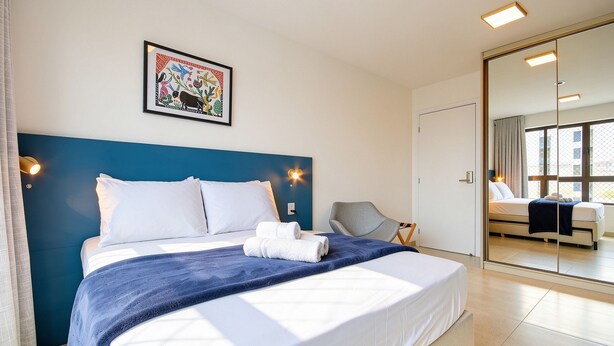 Une chambre d’hôtel avec un lit, une chaise, un grand miroir et un tableau accroché au mur.