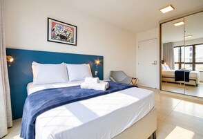 Quarto de hotel com uma cama, uma cadeira, um espelho grande e um quadro na parede.