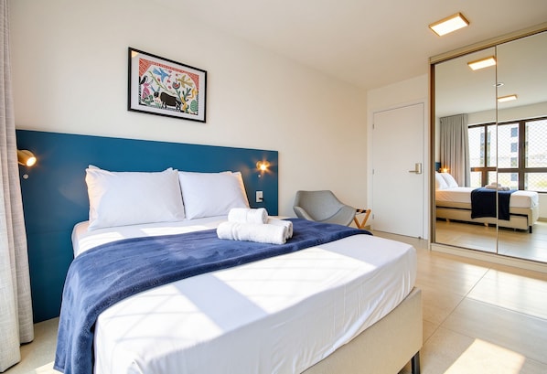 Une chambre d’hôtel avec un lit, une chaise, un grand miroir et un tableau accroché au mur.