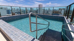 Une piscine sur le toit offrant une vue sur la ville, avec des garde-corps en métal et un revêtement de sol carrelé.