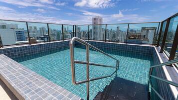 A rooftop swimming pool with a city view, metal railings, and tiled flooring.