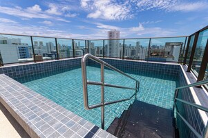 Piscina no terraço com vista para a cidade, grades de metal e piso revestido de azulejos.
