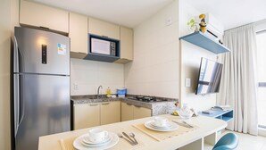 Une cuisine moderne équipée d’un réfrigérateur, d’un four à micro-ondes et d’une cuisinière à gaz. On y trouve une table à manger avec des chaises et un téléviseur fixé au mur.