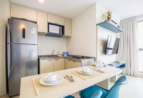 Cozinha moderna com geladeira, micro-ondas e fogão a gás. Há uma mesa de jantar com cadeiras e uma TV fixada na parede.