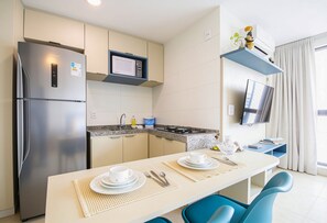 Une cuisine moderne équipée d’un réfrigérateur, d’un four à micro-ondes et d’une cuisinière à gaz. On y trouve une table à manger avec des chaises et un téléviseur fixé au mur.