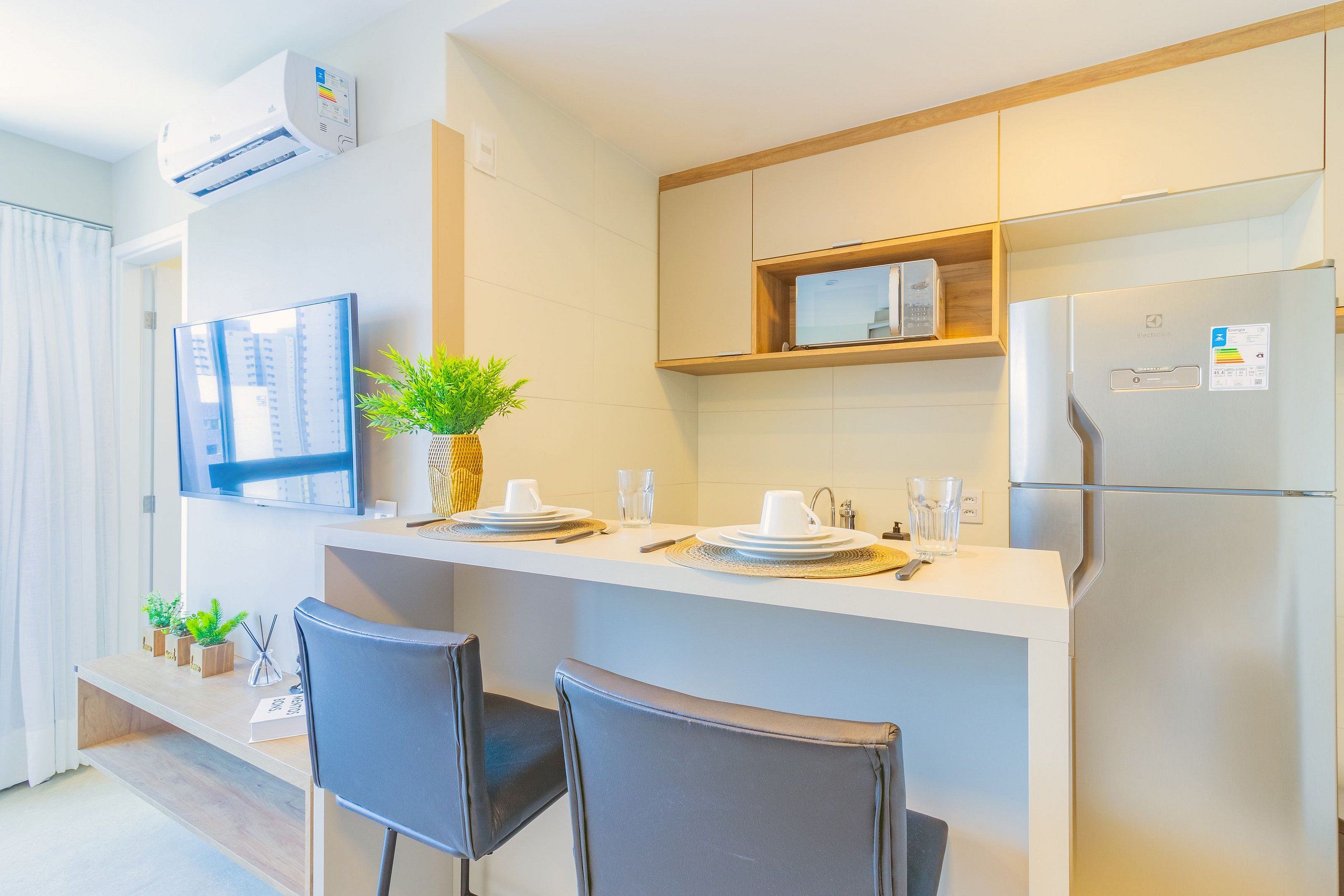Una cocina moderna con microondas integrado, refrigerador y un pequeño comedor con dos sillas y una planta.