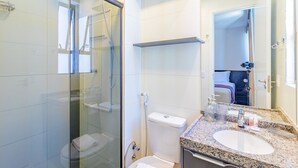 Ett modernt badrum med en duschavdelning med glasväggar, en vit toalett, en tvättställsskiva i granit och en spegel.