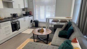 A modern living room with a grey sofa, a round coffee table, and a dining area with a white table and chairs.