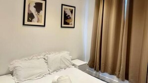 A bedroom with a bed, two framed pictures on the wall, and a window with curtains.