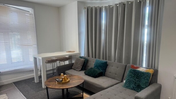A modern living room with a grey sectional sofa, a round coffee table, and a white desk with two chairs.