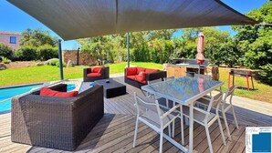 An outdoor patio with wicker furniture, a glass table, and a barbecue area.