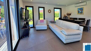 A modern living room with a white sofa, a television, and a dining area with a table and chairs.