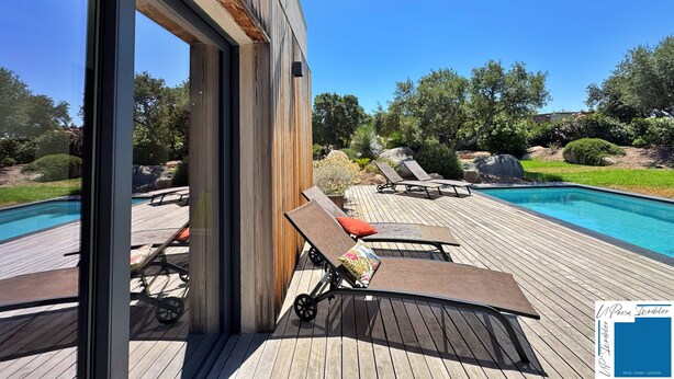 A modern outdoor pool area with wooden deck, lounge chairs, and a glass door leading to the pool.