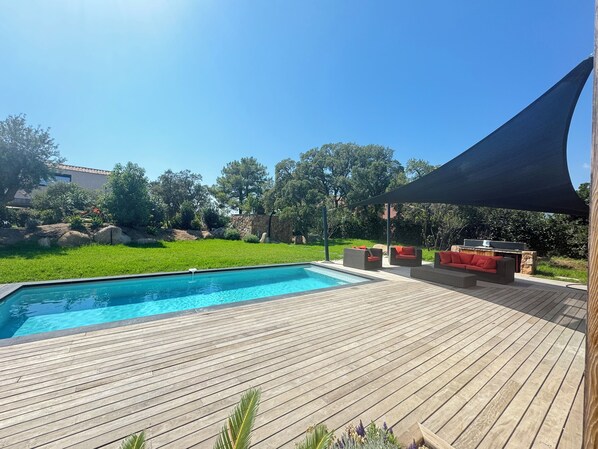A wooden deck with a swimming pool, outdoor furniture, and a shaded area.
