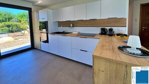 A modern kitchen with white cabinets, a wooden countertop, and a view of a garden through a large window.