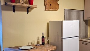 Une cuisine avec un réfrigérateur blanc, une table en bois sur laquelle se trouvent une bouteille de vin et des verres, et une horloge au mur.