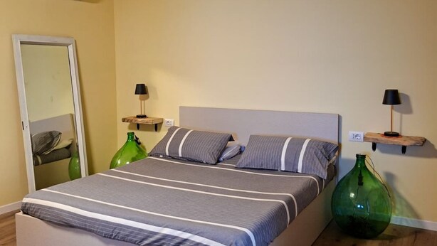 Une chambre à coucher avec un lit, des tables de chevet, des lampes, un miroir et un vase vert.