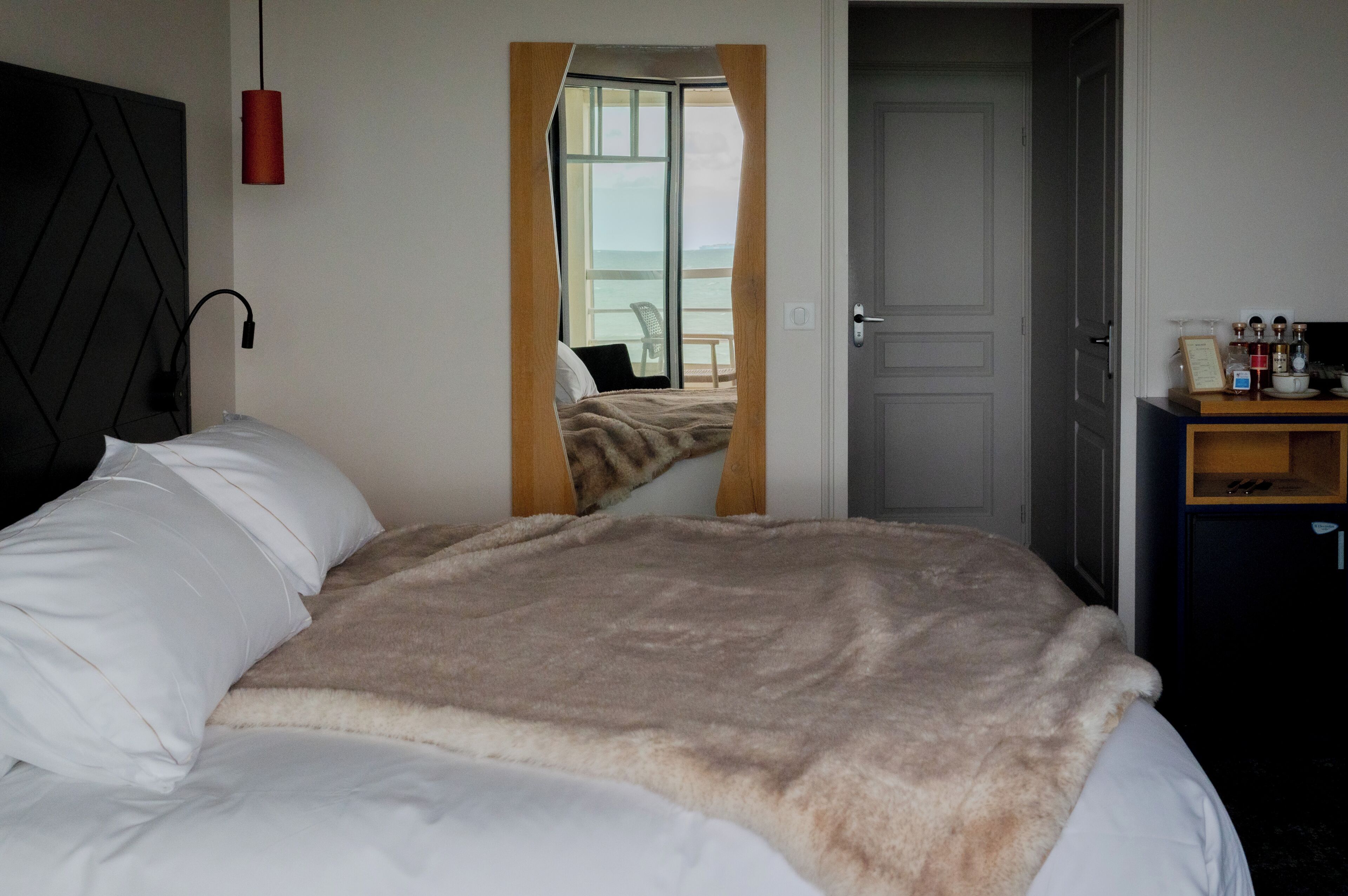 A bedroom with a bed, a nightstand with a lamp, a door, and a view of a balcony.