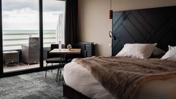 Habitación de hotel con cama, escritorio, silla y vista al océano, además de un amplio ventanal.