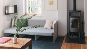 Un salon chaleureux avec un canapé gris, une table basse en bois sur laquelle sont posés un livre et un vase, une cheminée et un téléviseur fixé au mur.