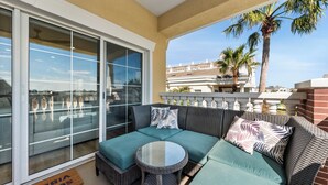 A balcony with a wicker sofa, a glass table, and a view of palm trees and a cruise ship. - Beautiful Condo with Golf Course Views, Kids Bedroom and Near Attractions (Kissimmee)