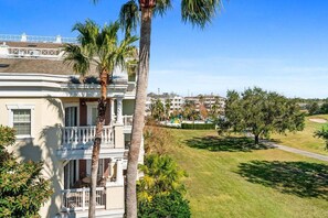 A multi-story building with a balcony, palm trees, and a golf course in the background. - Beautiful Condo with Golf Course Views, Kids Bedroom and Near Attractions (Kissimmee)