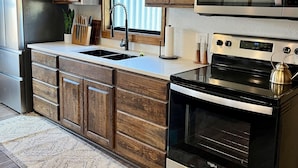 Una cocina con armarios de madera, un refrigerador de acero inoxidable, un microondas, una estufa y un lavamanos.
