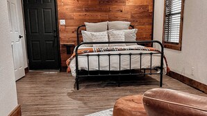 Un dormitorio con cabecera de madera, cama con ropa de cama blanca, reposapiés marrón y alfombra estampada.