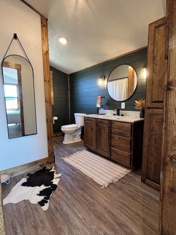 Une salle de bain avec un meuble-lavabo en bois, un miroir rond, des toilettes et un tapis en peau de vache.