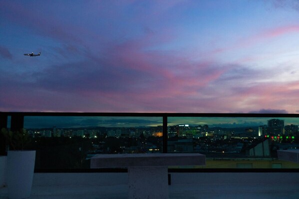 A cityscape at dusk with an airplane flying in the sky.