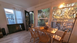 Un comedor con una mesa y sillas de madera, un ventanal con vistas a árboles y una puerta negra que da al exterior.