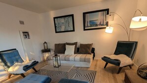 Una sala de estar moderna con un sofá, un reposapiés y sillones, una mesa de centro y dos lámparas de pared.