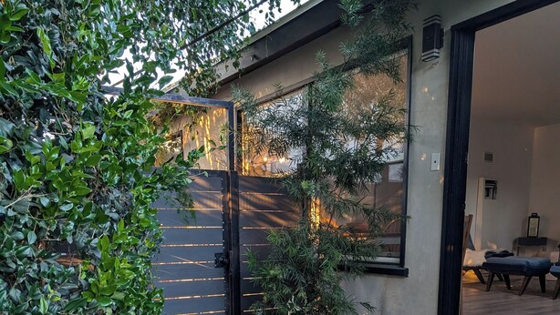 Una entrada empavedada con escalones que conducen a una puerta, rodeada de vegetación.