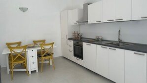 A modern kitchen with white cabinets, a black countertop, and a stainless steel sink. There is a dining table with two chairs and a kettle on the counter. - Chez Elena with shared terrace overlooking the sea Ravello (Ravello)