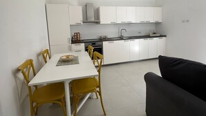 A compact kitchen with white cabinets, a black countertop, and a dining area with a white table and yellow chairs. - Chez Elena with shared terrace overlooking the sea Ravello (Ravello)