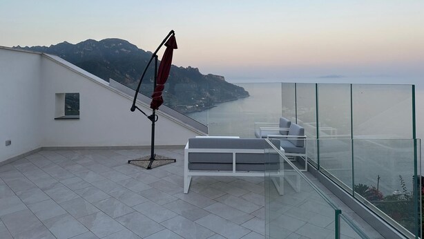 A rooftop terrace with a glass balustrade, a red umbrella, and two white lounge chairs. - Chez Elena with shared terrace overlooking the sea Ravello (Ravello)