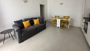 A modern living room with a grey sofa, yellow cushions, a small round table, and a dining area with a white table and yellow chairs. - Chez Elena with shared terrace overlooking the sea Ravello (Ravello)