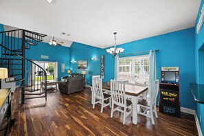 A dining area with a wooden table and chairs, a chandelier, and a Pac-Man arcade machine.