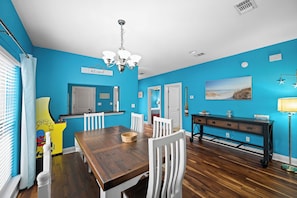 A dining area with a wooden table, white chairs, a black console table, and a ceiling light fixture.
