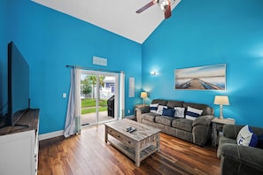 A living room with a blue wall, a wooden coffee table, a sofa, and a painting. - 🏝️Gated Community-Great Amenities-Coral Retreat🌊 (Pensacola)