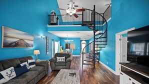 Ein Wohnzimmer mit blauer Wand, einem Holztisch, einer Couch, einem TV-Schrank und einer Treppe.
