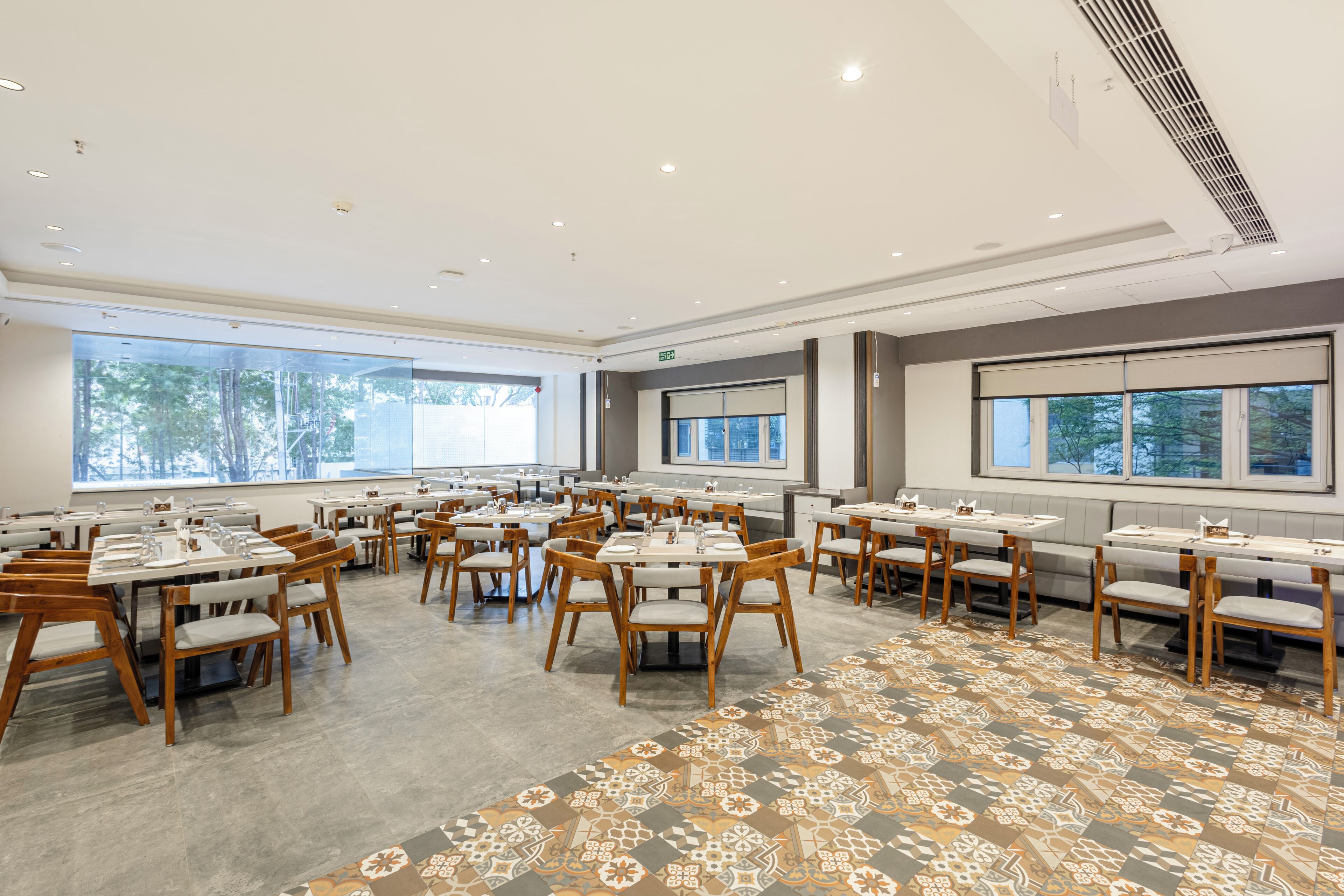 Un comedor amplio con varias mesas y sillas, ventanas grandes y una alfombra estampada.
