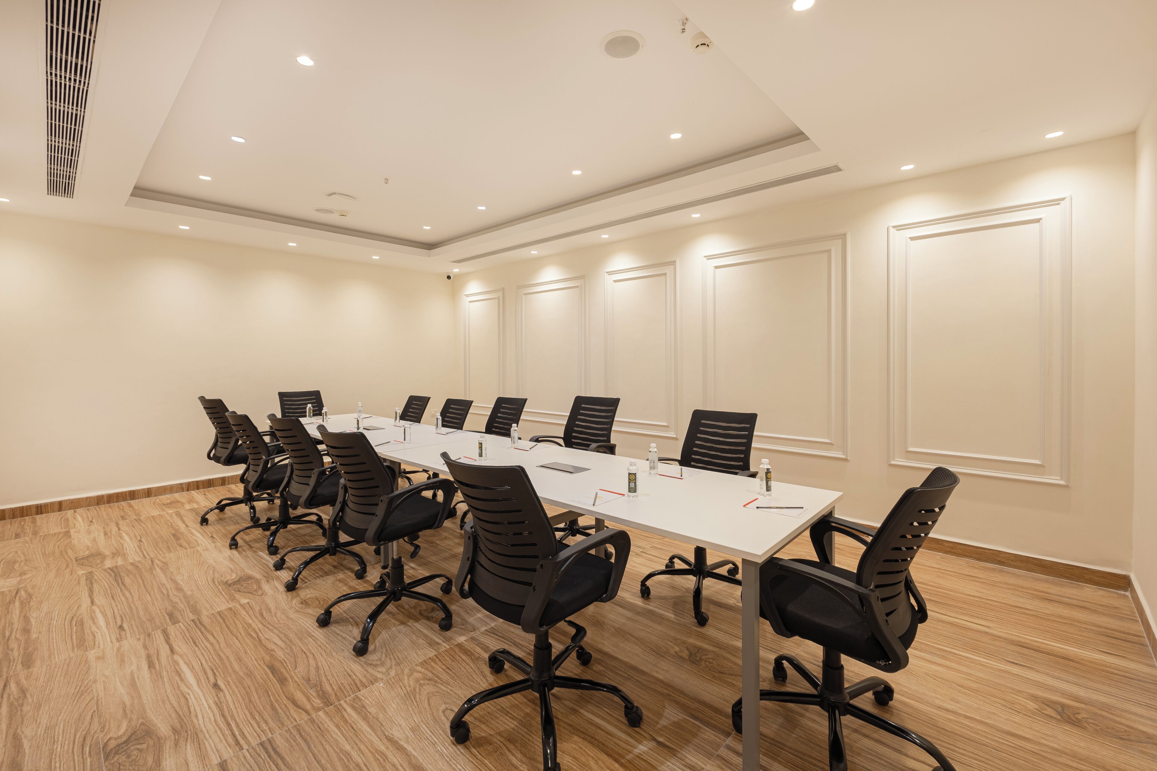 Sala de conferência com uma mesa comprida, cadeiras pretas e iluminação embutida no teto.