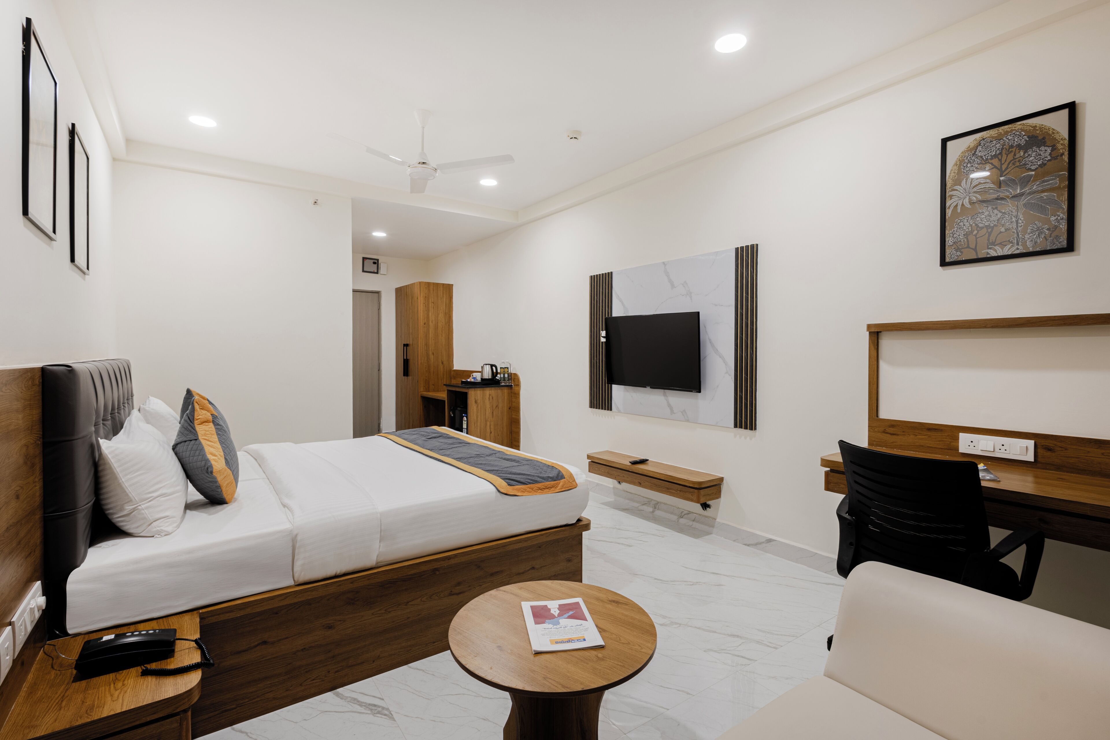 Habitación de hotel moderna con cama, mesita de noche, escritorio, silla y televisión en la pared.