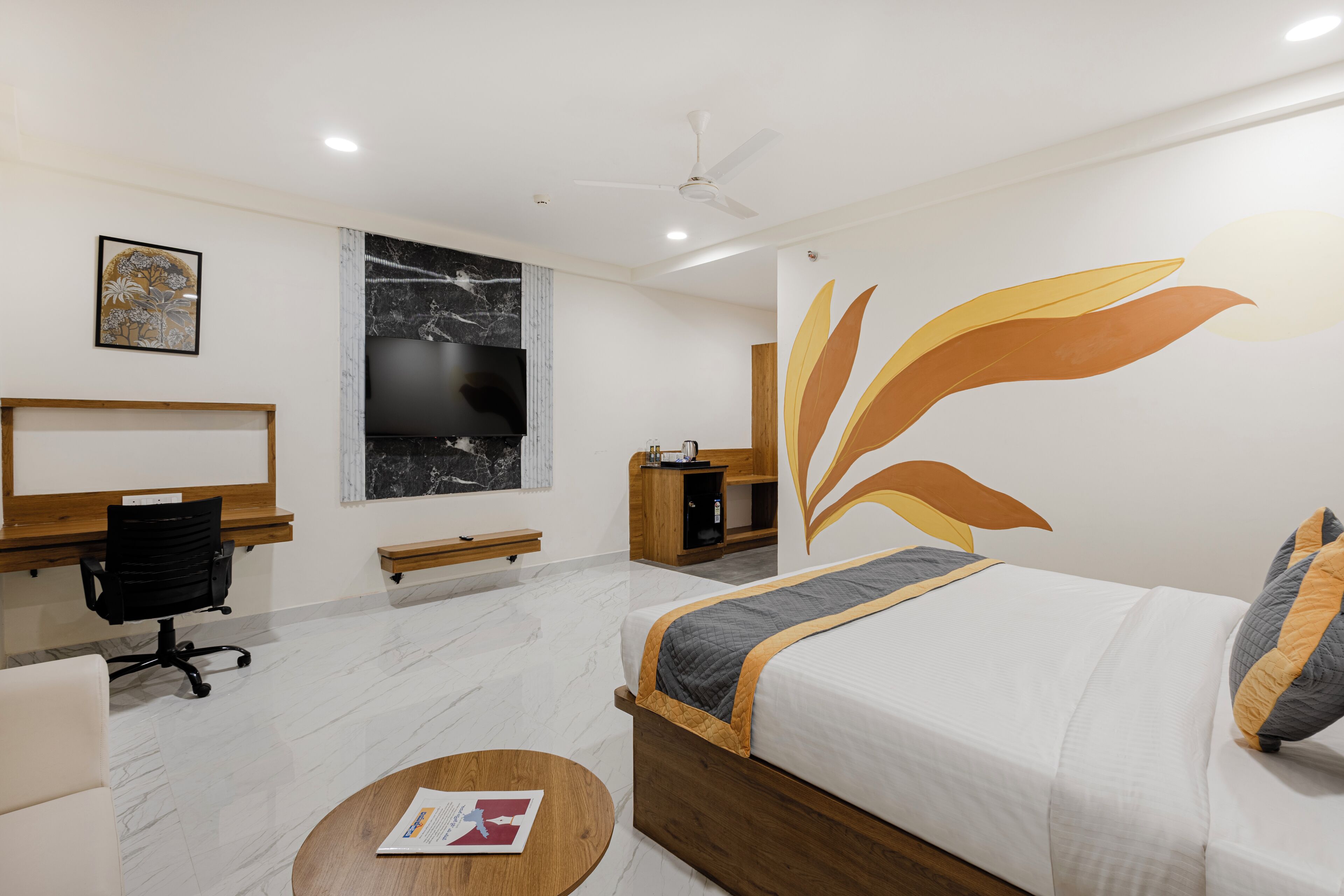 A hotel room with a bed, a desk, a chair, a TV, and a wall with a leaf design.